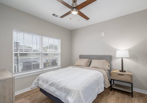 A bedroom with a bed, nightstand, and window with blinds.