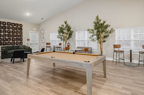 A pool table in the middle of a room with a green couch and a tree.