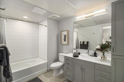 A bathroom with a white tiled shower, a white toilet, a sink with a mirror, and a towel hanging on the shower rod.
