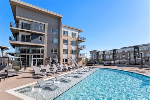 A large swimming pool with lounge chairs in front of a modern apartment building.