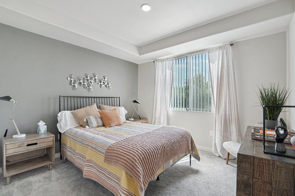 A bedroom with a bed, nightstand, and a plant.