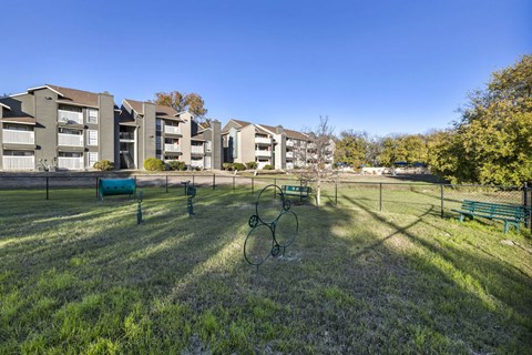 A grassy area with a basketball hoop in front of apartment buildings.