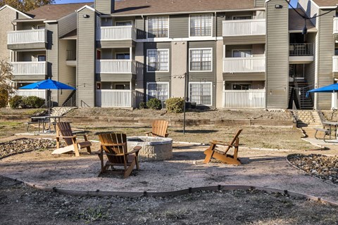 A patio area with chairs and umbrellas in front of apartment buildings.