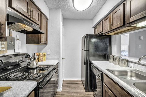 A black refrigerator is in the corner of a kitchen with wooden cabinets.