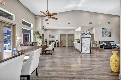 A yellow vase sits on a wooden floor in a spacious room with white chairs and a white reception desk.