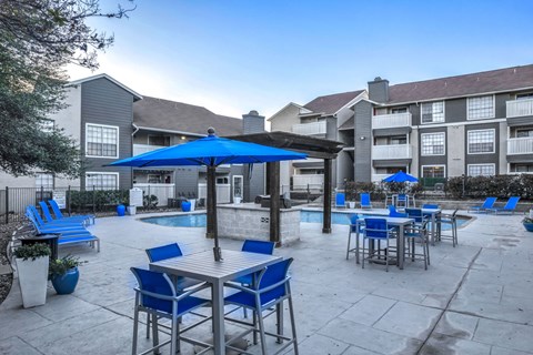A patio with blue chairs and tables is surrounded by apartment buildings.