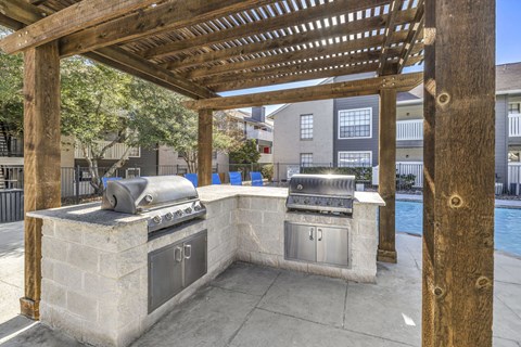 A wooden pergola over an outdoor kitchen with a grill and sink.