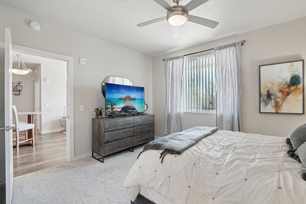 A bedroom with a large bed, a flat screen TV, and a ceiling fan.