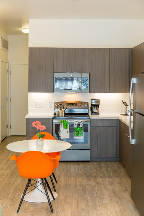 A modern kitchen with a white table and orange chairs.