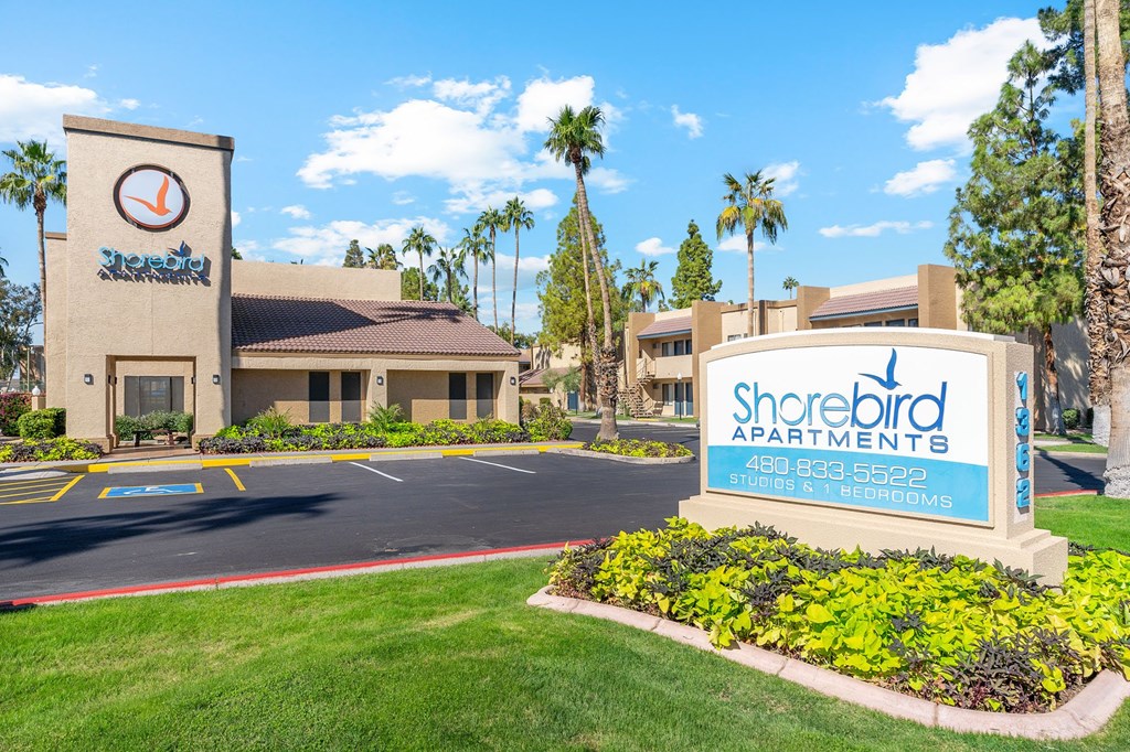 A sign for Shorebird Apartments is in front of a building with palm trees in the background.