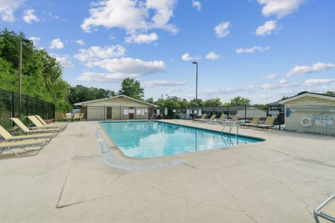 A large outdoor swimming pool surrounded by a fence and lounge chairs.