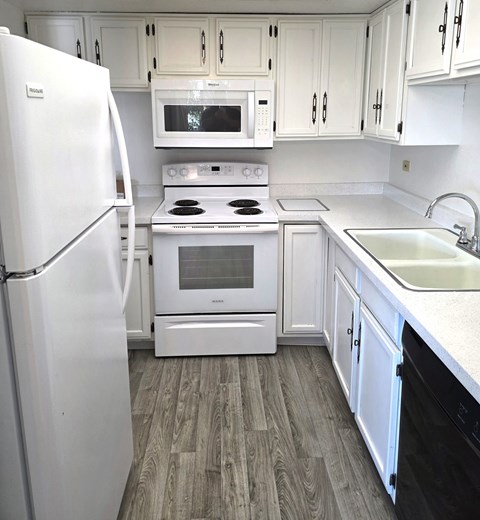 A white kitchen with a fridge, microwave, oven, and sink.