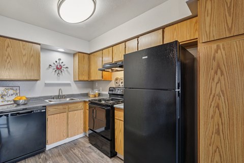 A black refrigerator stands in a kitchen with wooden cabinets.