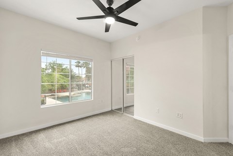 A room with a ceiling fan and a window overlooking a pool.