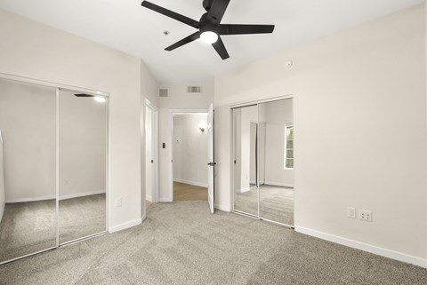 A spacious room with a ceiling fan and glass doors leading to a balcony.