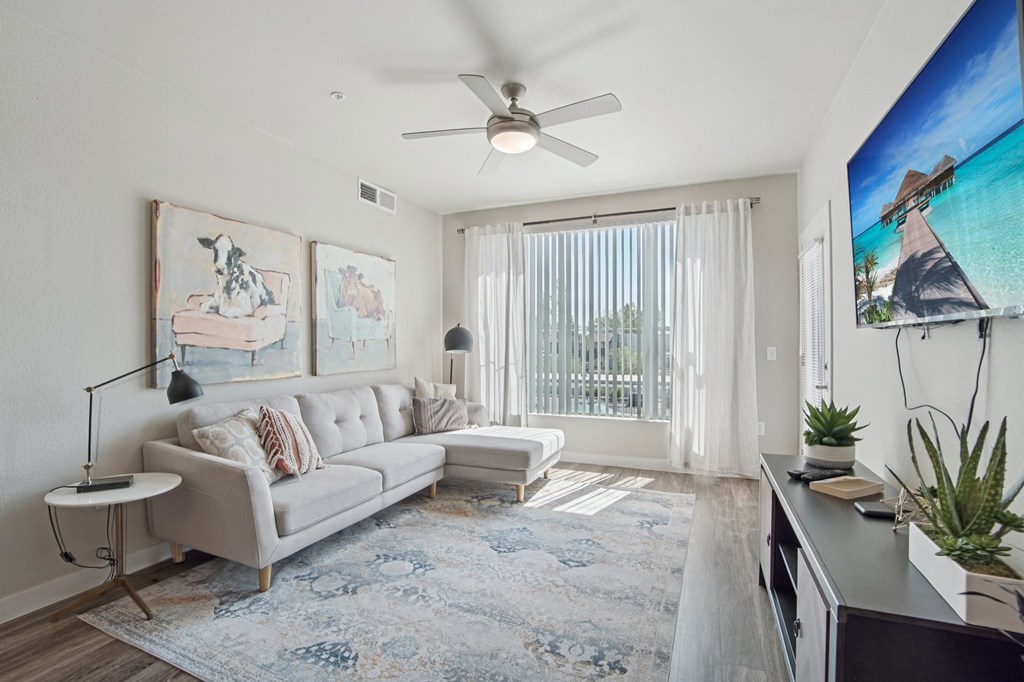 A living room with a grey sofa, a small table, a rug, a ceiling fan, and a painting on the wall.