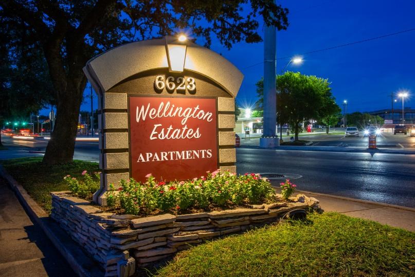 A sign for Wellington Estates Apartments is lit up at night.