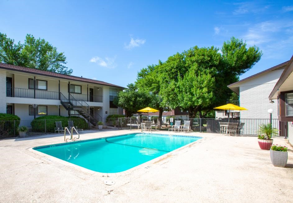 A swimming pool in front of a building with a yellow umbrella.