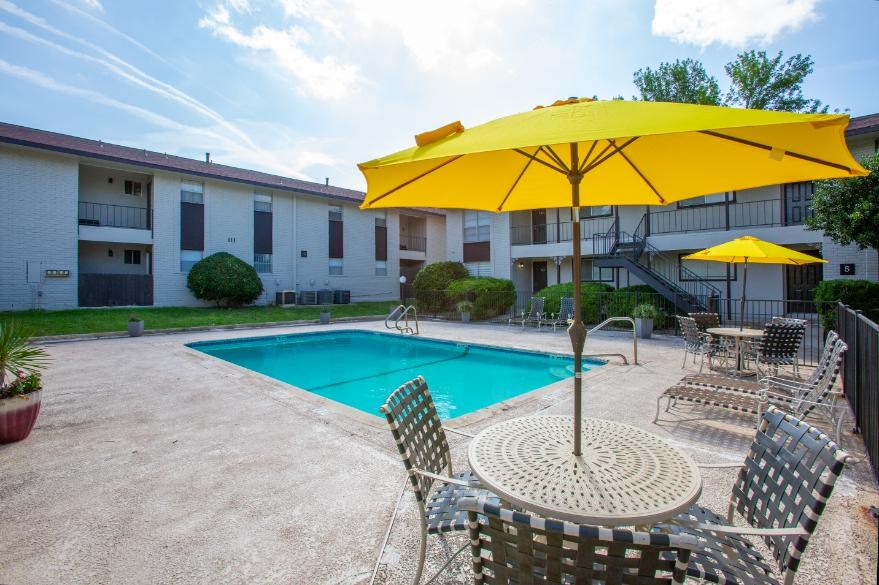 A yellow umbrella is over a table with chairs around a pool.