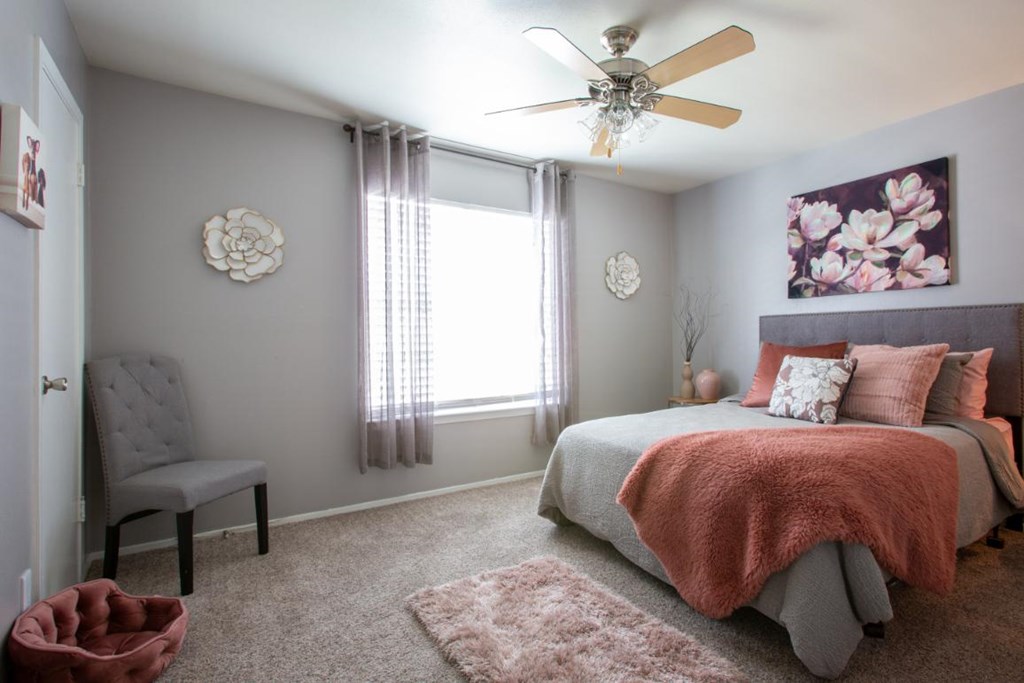 A bedroom with a bed, chair, and a ceiling fan.