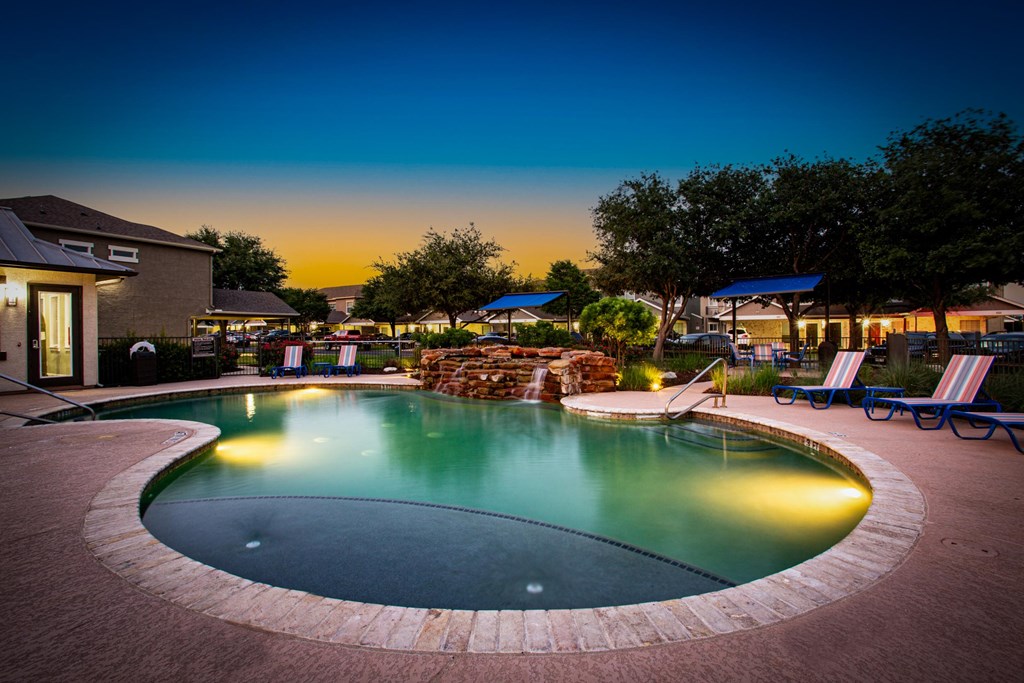 A pool surrounded by a brick patio at dusk.