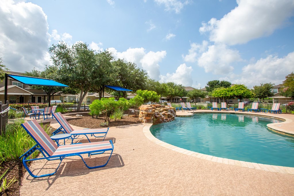 A pool with a blue umbrella and a bench.