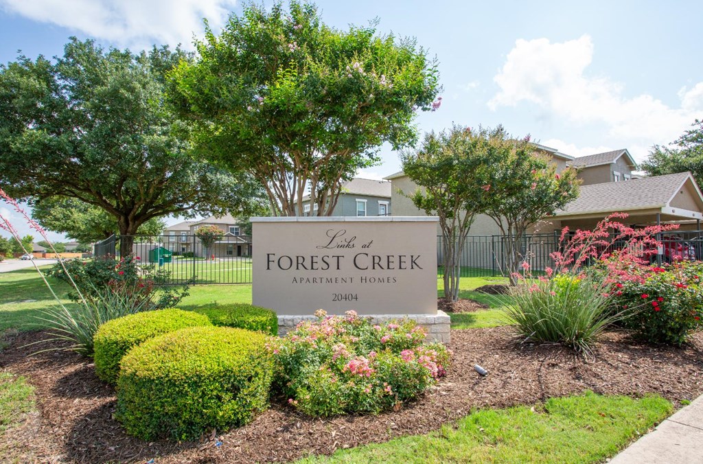 A sign for Forest Creek Apartment Homes is surrounded by greenery and flowers.