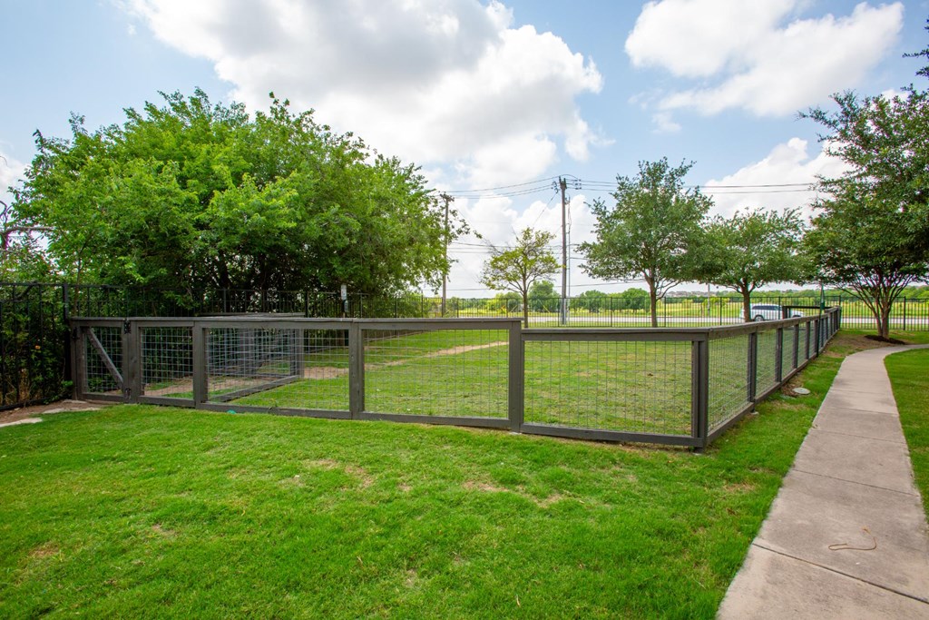 A fenced green field with trees and a cloudy sky.
