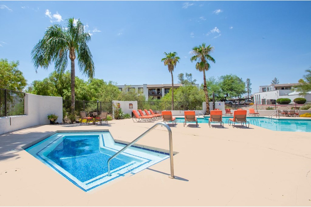 A pool surrounded by palm trees and orange chairs.