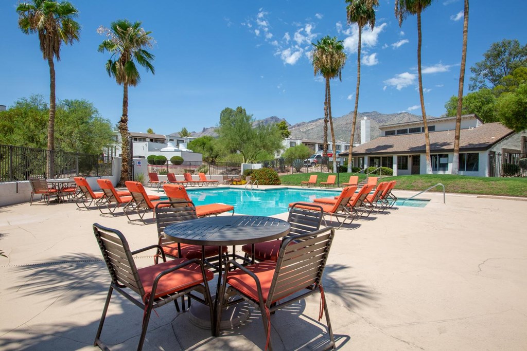 A table and chairs set up on a patio with a pool and palm trees in the background.