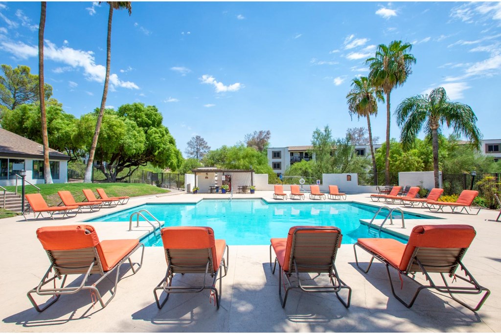 A pool surrounded by orange chairs and palm trees.