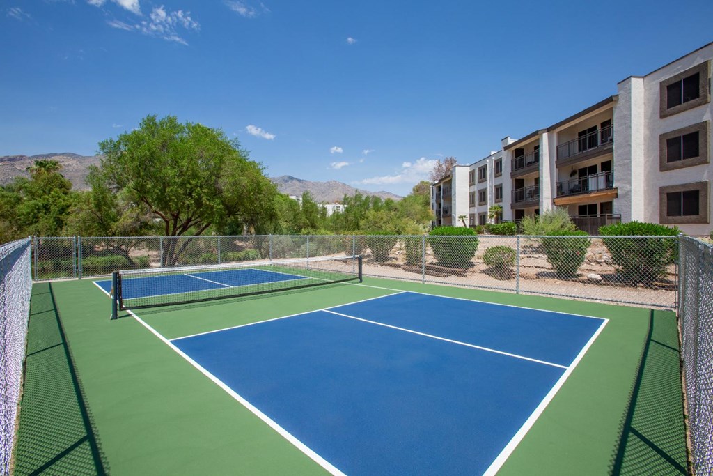 A tennis court with a green fence and a building in the background.