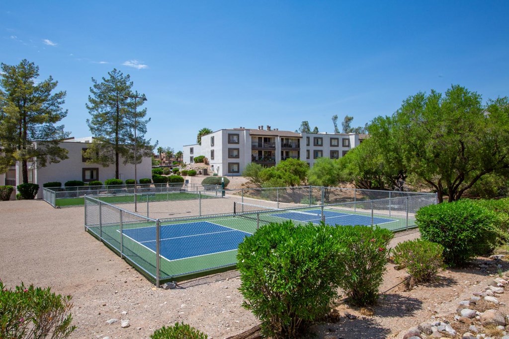 A tennis court surrounded by trees and bushes with a building in the background.