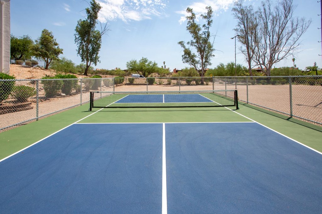 A tennis court with a net in the middle and a fence surrounding it.
