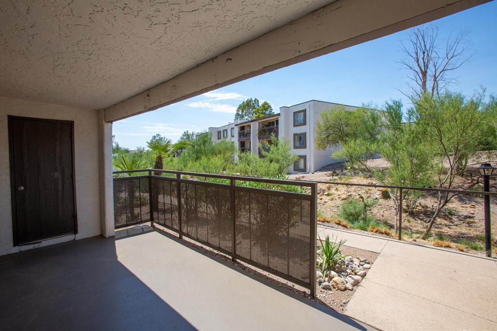 A balcony with a black railing overlooks a building and greenery.