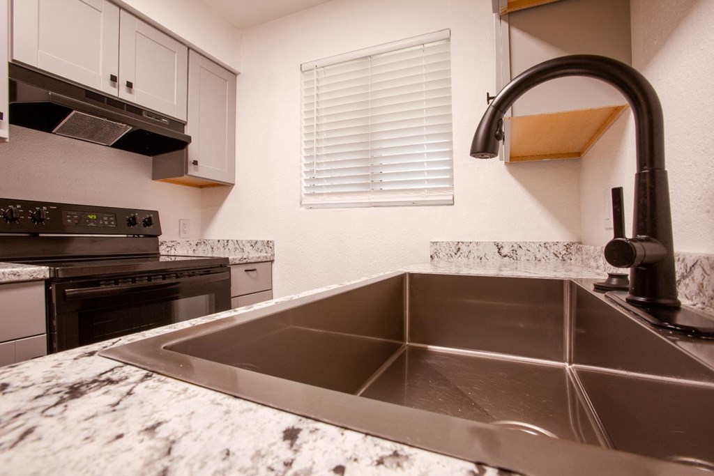 A kitchen with a stainless steel sink and marble countertop.
