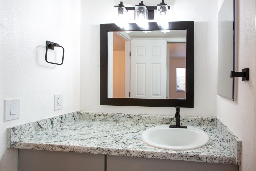 A bathroom sink with a marble counter top and a rectangular mirror above it.