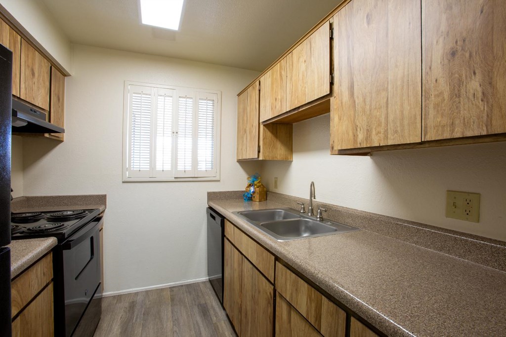 A kitchen with wooden cabinets and a window with blinds.