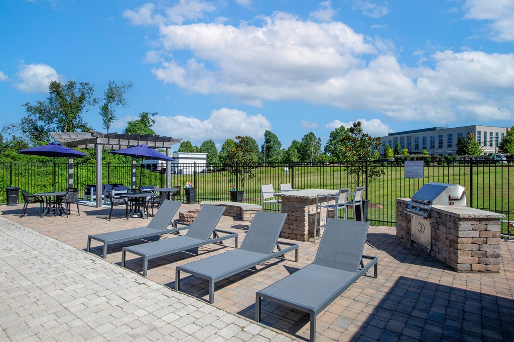 A patio with grey chairs and tables is surrounded by a black fence.