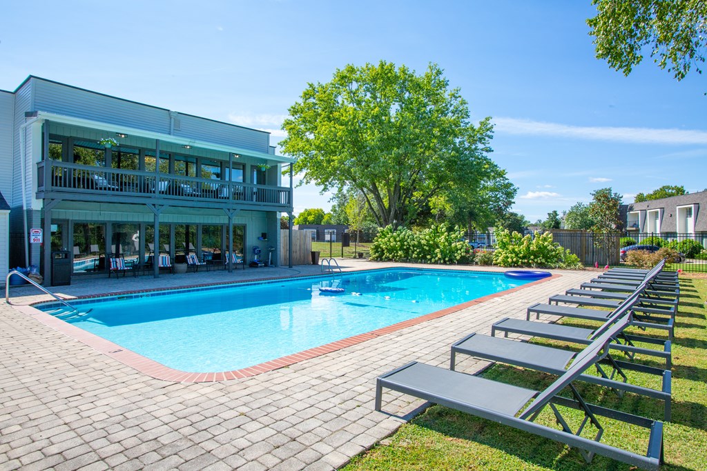 A pool with a building behind it and benches along the side.