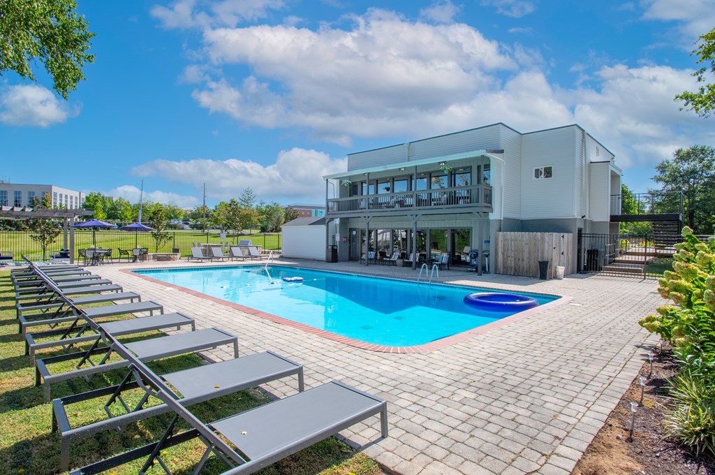 A pool with a building behind it and sun loungers in front.