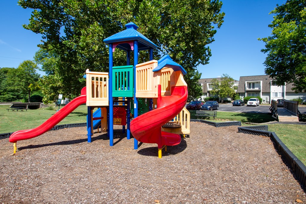A playground with a red slide and a blue and yellow playhouse.