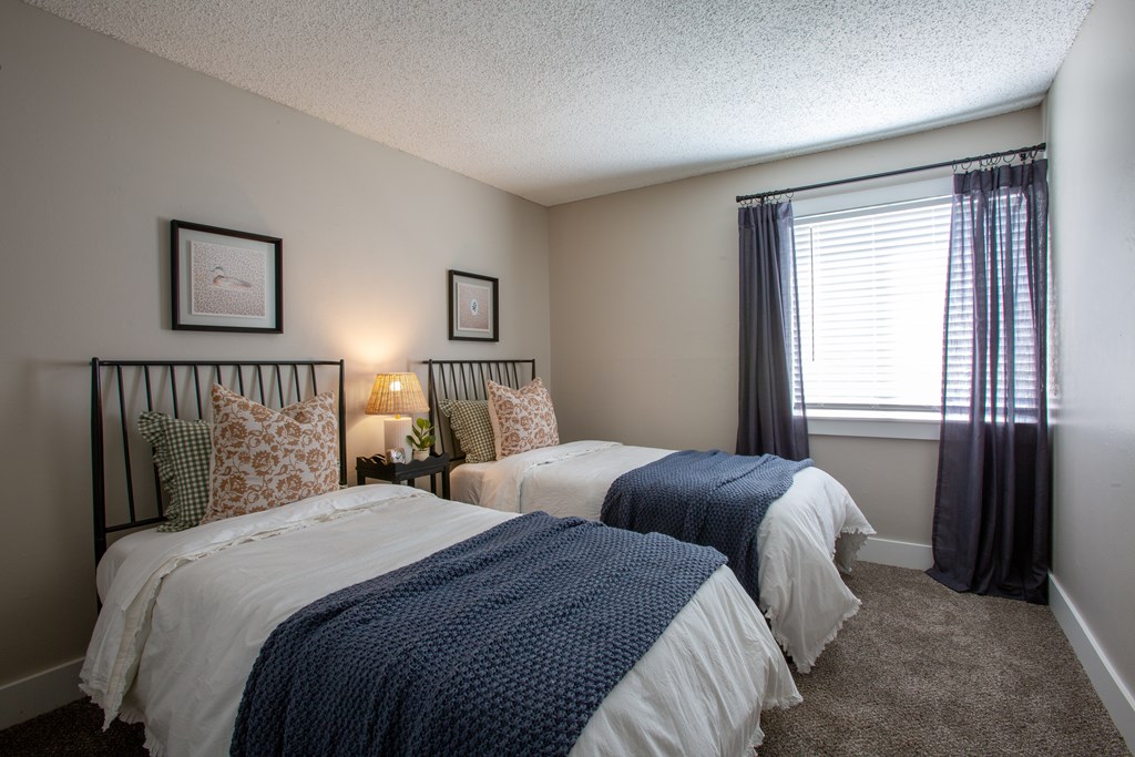 Two twin beds with blue and white bedspreads in a room with two wall lamps.