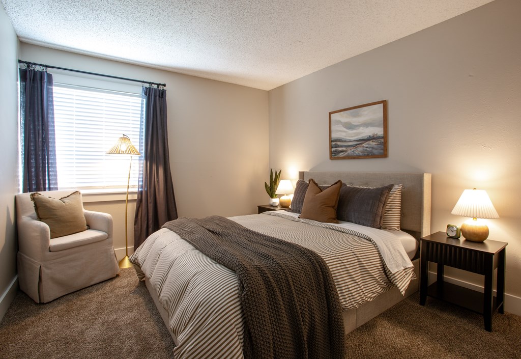 A bedroom with a bed, chair, and lamp.