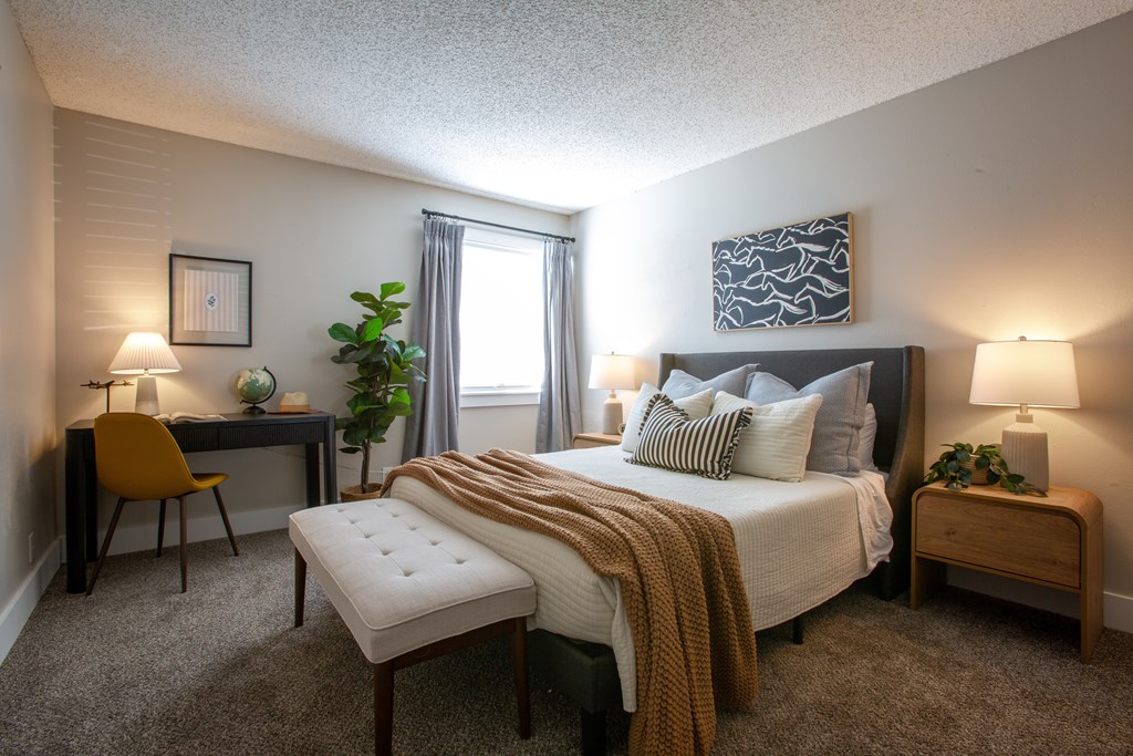 A bedroom with a bed, desk, chair, and two lamps.