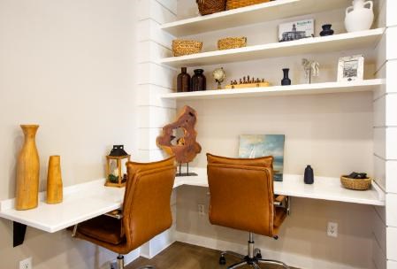Two chairs sit on a white desk with shelves above filled with decorative items.