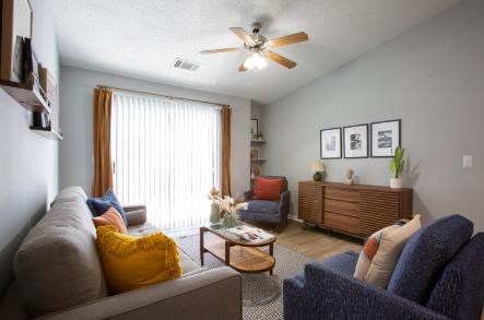 A living room with a grey couch, a blue couch, a wooden coffee table, and a ceiling fan.