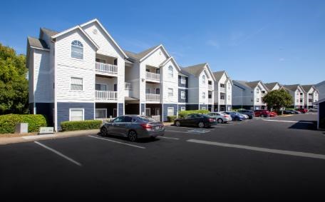 A row of white and blue apartment buildings with cars parked in front.