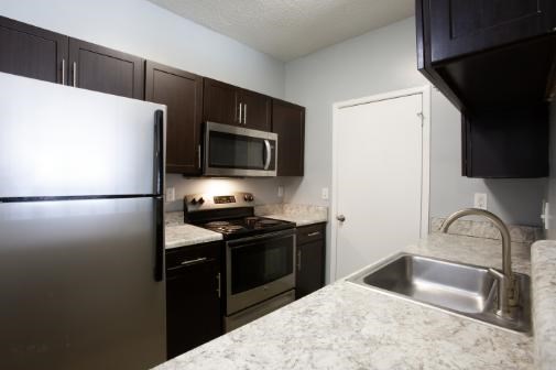 A kitchen with a refrigerator, microwave, oven, sink and cabinets.