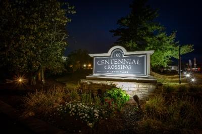 A sign that says Centennial Crossing stands in front of a grassy area.